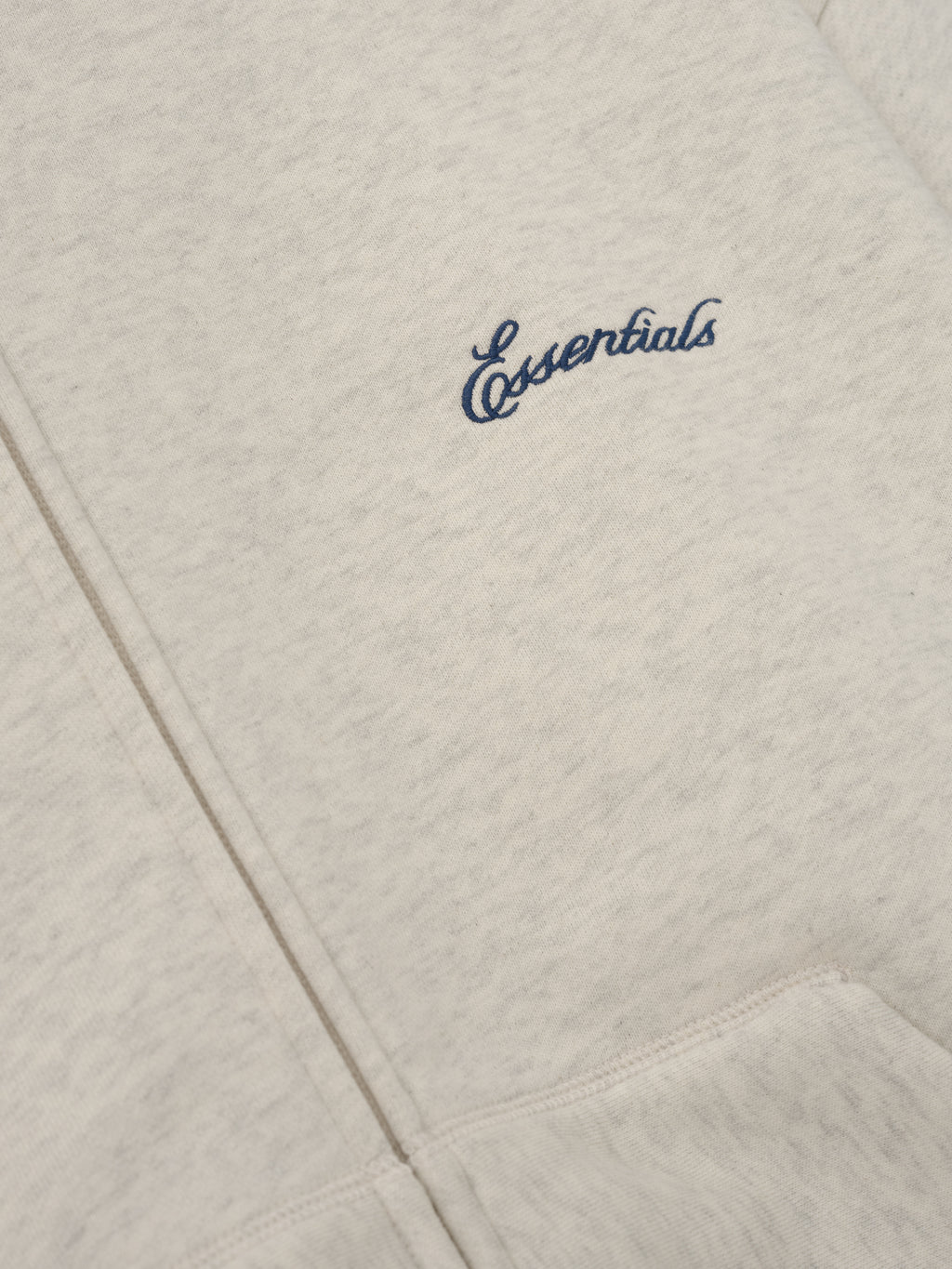 Signature Classic Zip Up Hoodie in light gray with navy Essentials chest logo and detailed kangaroo pocket stitching shown in close up as Tops