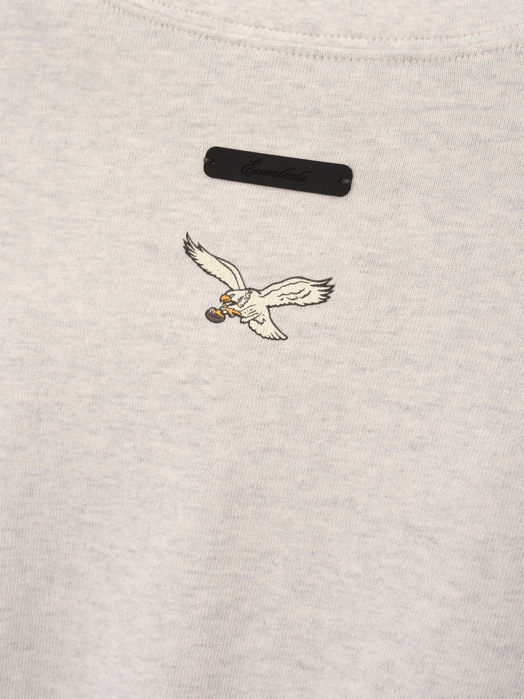 Eagles Merch Tee cream fabric close up with embroidered flying eagle emblem and black chest label in a detailed Tops product view