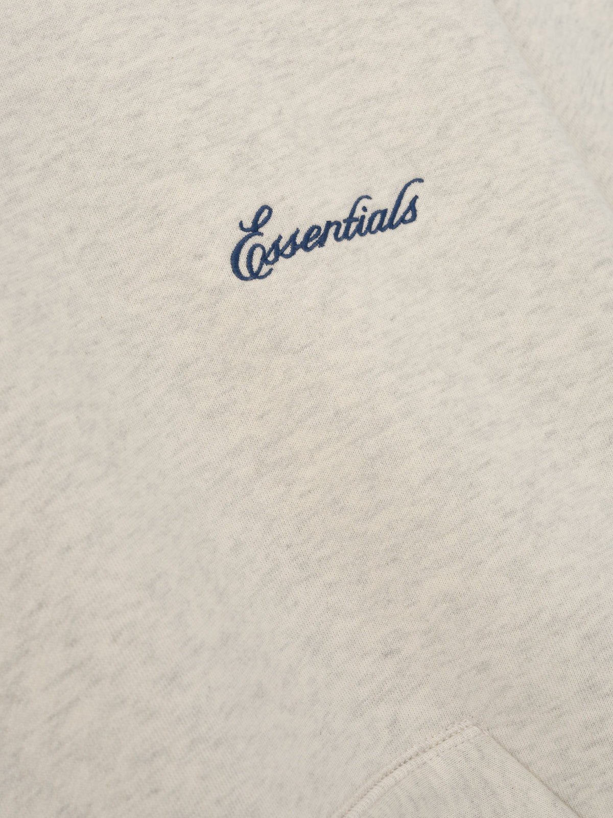 Signature Classic Hoodie in light taupe with blue Essentials script branding on soft textured fabric and a close view of the kangaroo pocket seam as Tops