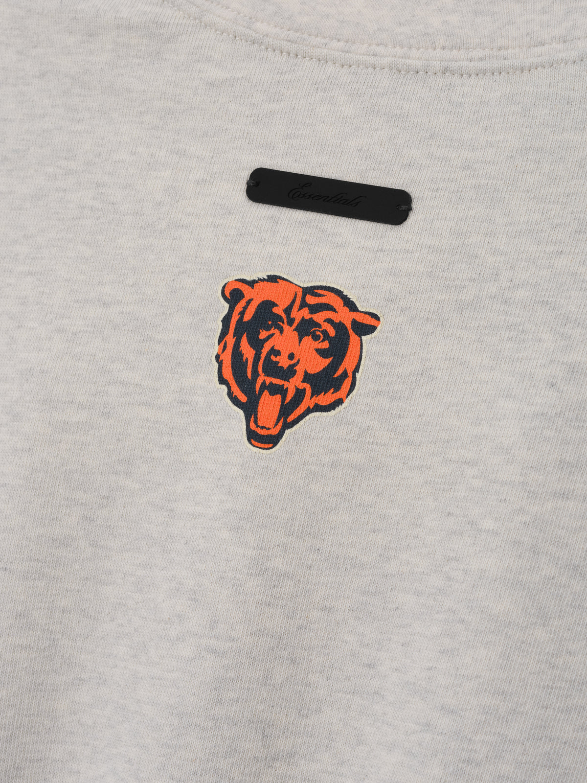 Bears Merch Tee gray fabric close up featuring an orange and black bear head emblem with a black Fear of God label in a detailed Tops product view