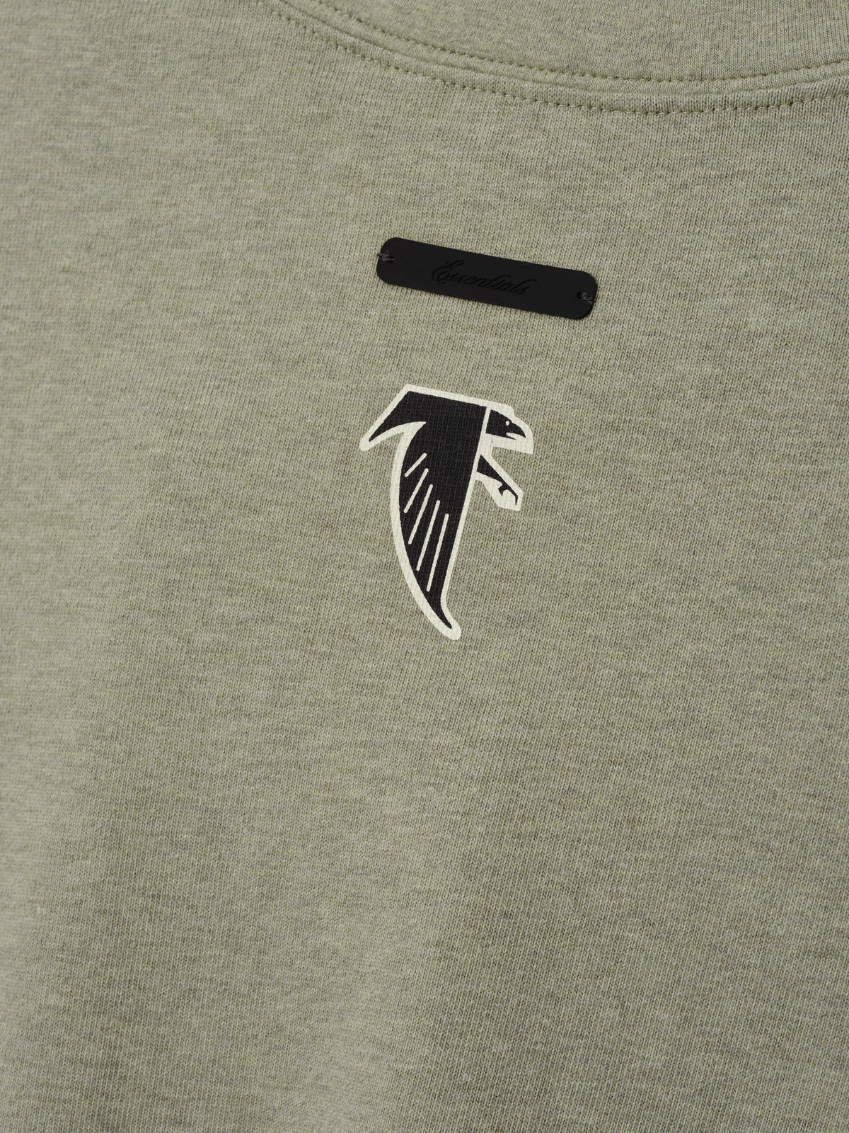 Falcons Merch Tee olive green fabric close up featuring a black and white falcon emblem with a black chest label in a detailed Tops product view