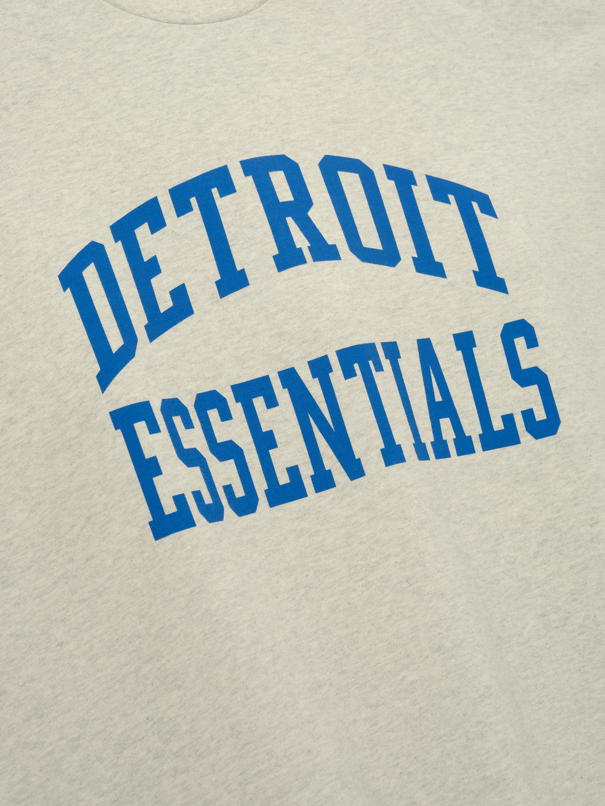 Lions Merch Tee cream fabric close up featuring bold blue Detroit Essentials collegiate lettering in a detailed Tops product view