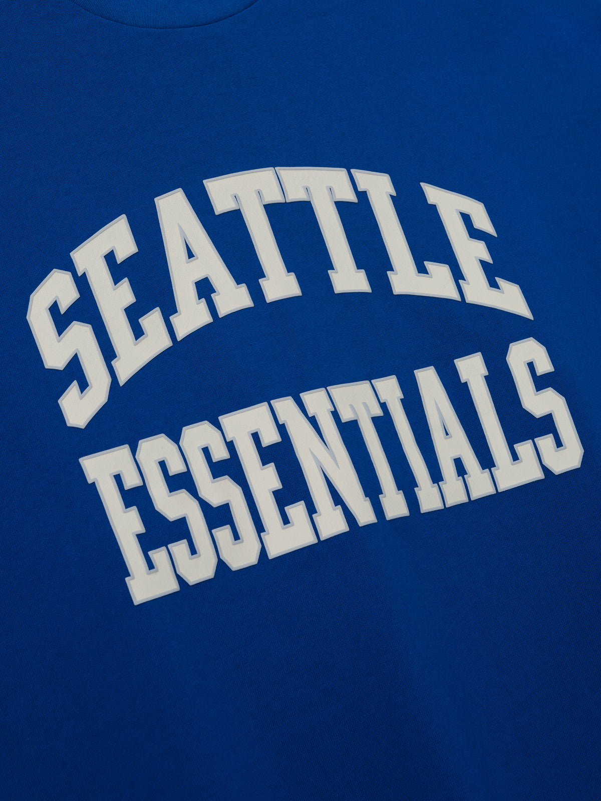 Seahawks Merch Tee blue fabric close up featuring bold white Seattle Essentials collegiate lettering in a detailed Tops product view