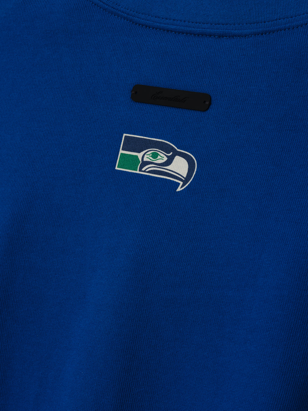 Seahawks Merch Tee blue fabric close up featuring a Seattle Seahawks logo and black chest label in a detailed Tops product view