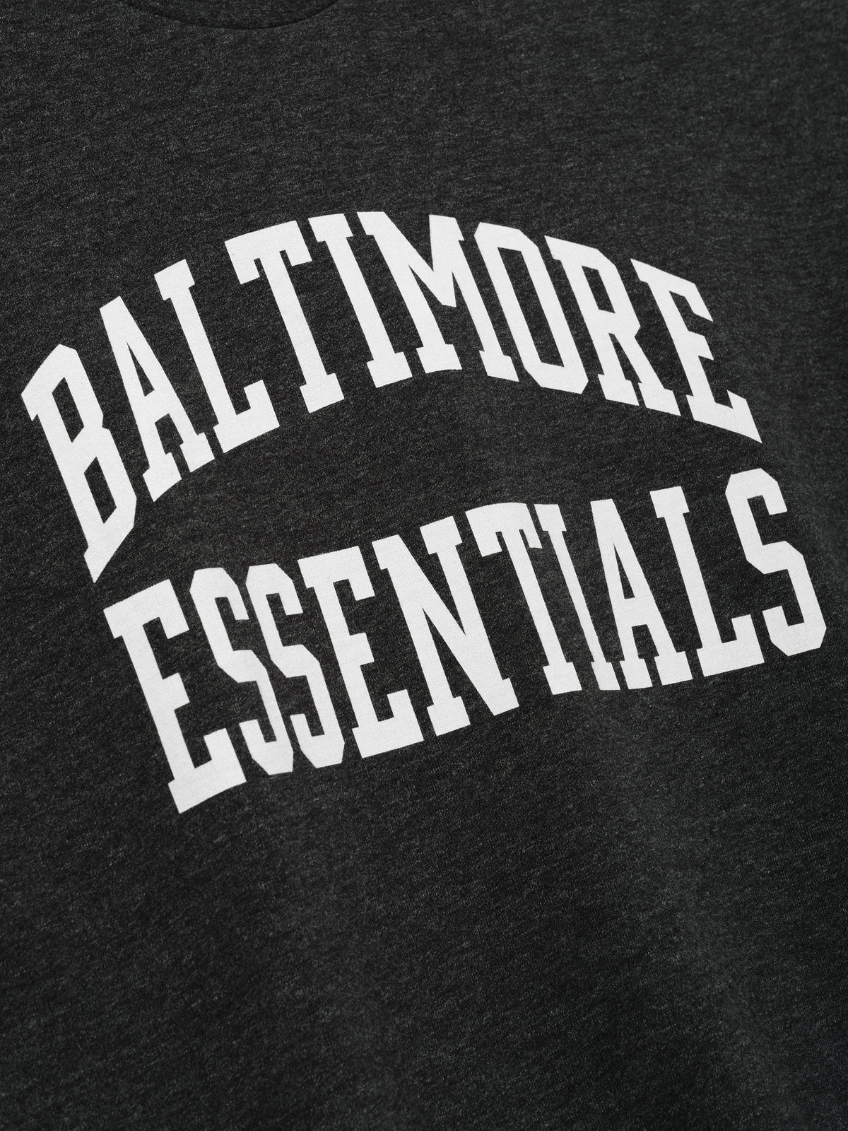 Ravens Merch Tee dark charcoal fabric close up with bold white Baltimore Essentials collegiate lettering in a detailed Tops product view