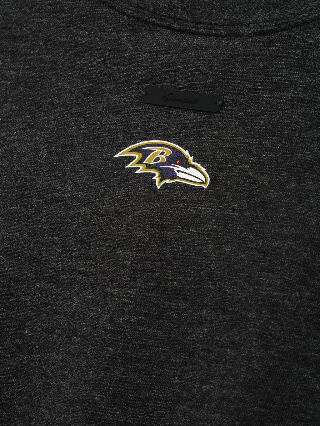 Ravens Merch Tee dark charcoal fabric close up with an embroidered Baltimore Ravens bird logo and subtle black label in a detailed Tops product view
