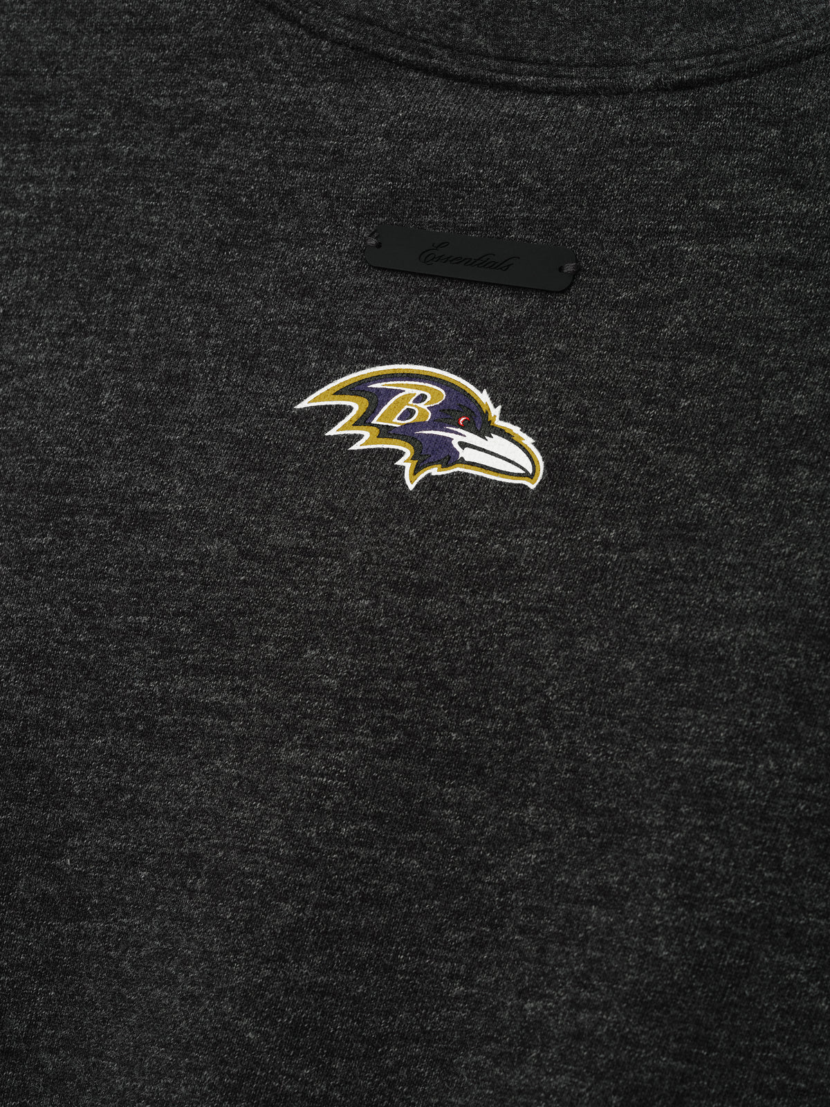 Ravens Merch Tee dark charcoal fabric close up with an embroidered Baltimore Ravens bird logo and subtle black label in a detailed Tops product view