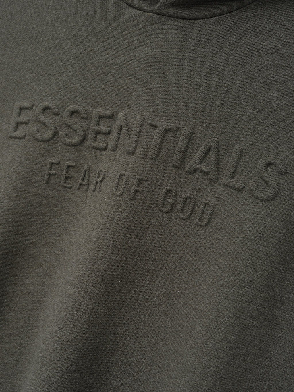 Embossed FW26 90s Relaxed Hoodie close up in dark gray showing tonal raised Essentials Fear of God lettering across the chest and soft fleece texture
