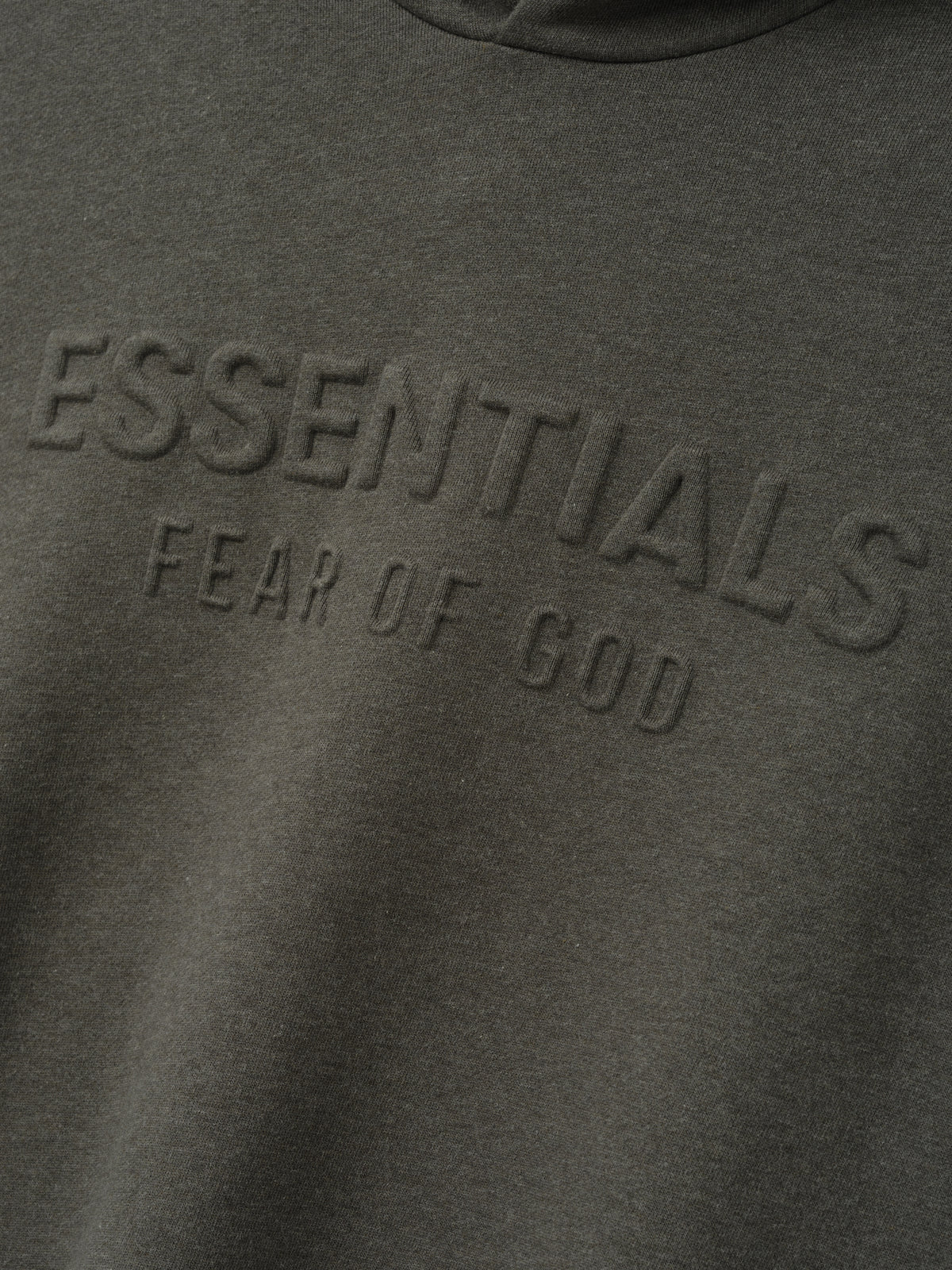 Embossed FW26 90s Relaxed Hoodie close up in dark gray showing tonal raised Essentials Fear of God lettering across the chest and soft fleece texture