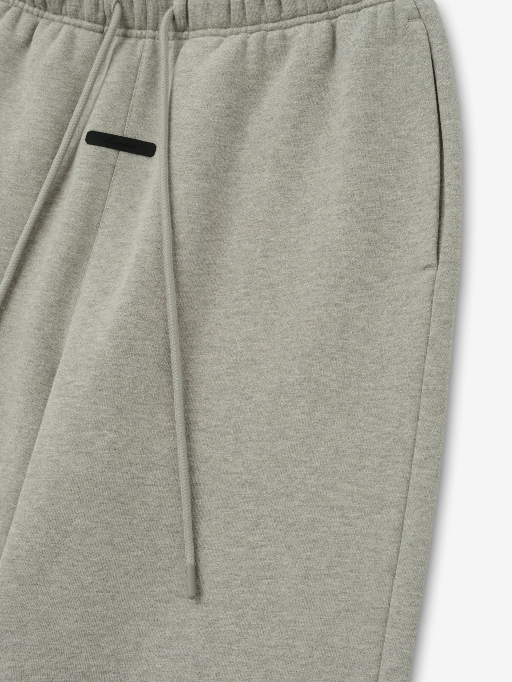 Essentials FW26 Classic Trackpant in light gray close up showing an elastic waistband drawstring and black zip pocket detail against a plain white background