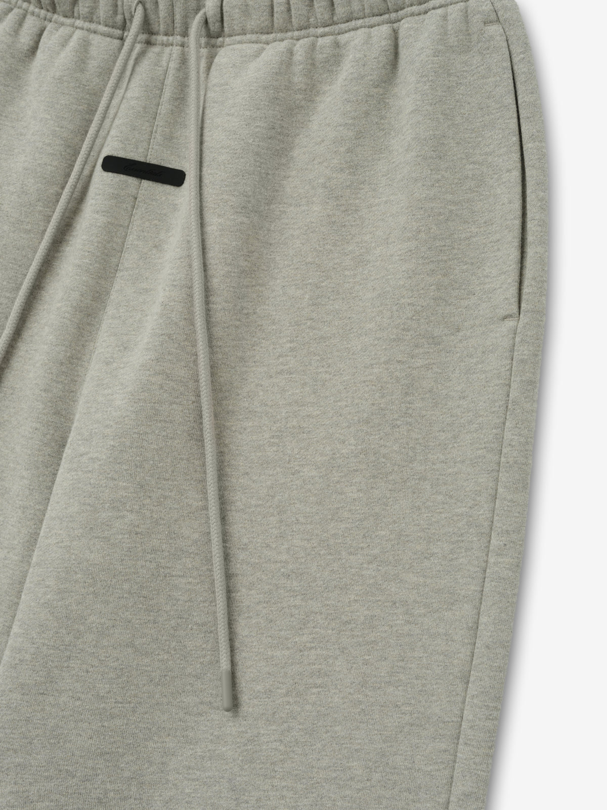 Essentials FW26 Classic Trackpant in light gray close up showing an elastic waistband drawstring and black zip pocket detail against a plain white background