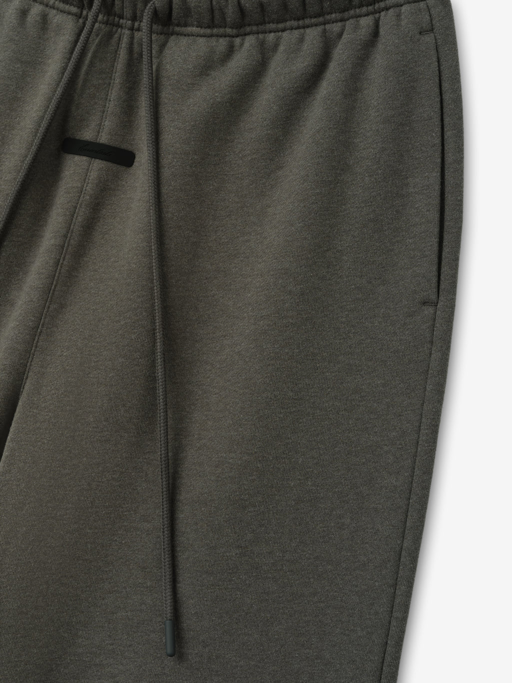 Essentials FW26 Classic Trackpant in dark gray close up showing an elastic waistband drawstring and black zip pocket detail against a plain white background