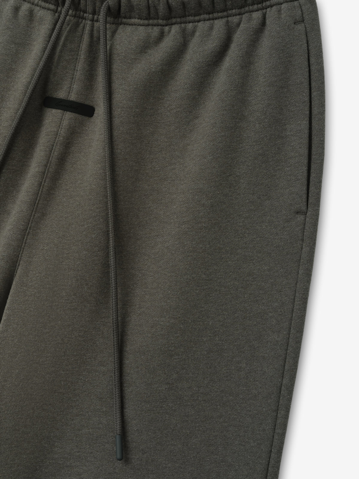 Essentials FW26 Classic Trackpant in dark gray close up showing an elastic waistband drawstring and black zip pocket detail against a plain white background