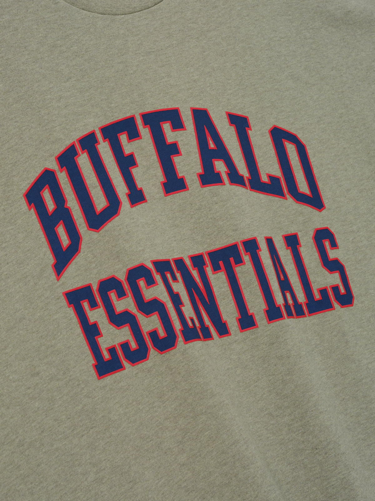 Bills Merch Tee olive green fabric close up featuring bold Buffalo Essentials collegiate lettering in red and blue shown as a detailed Tops product view