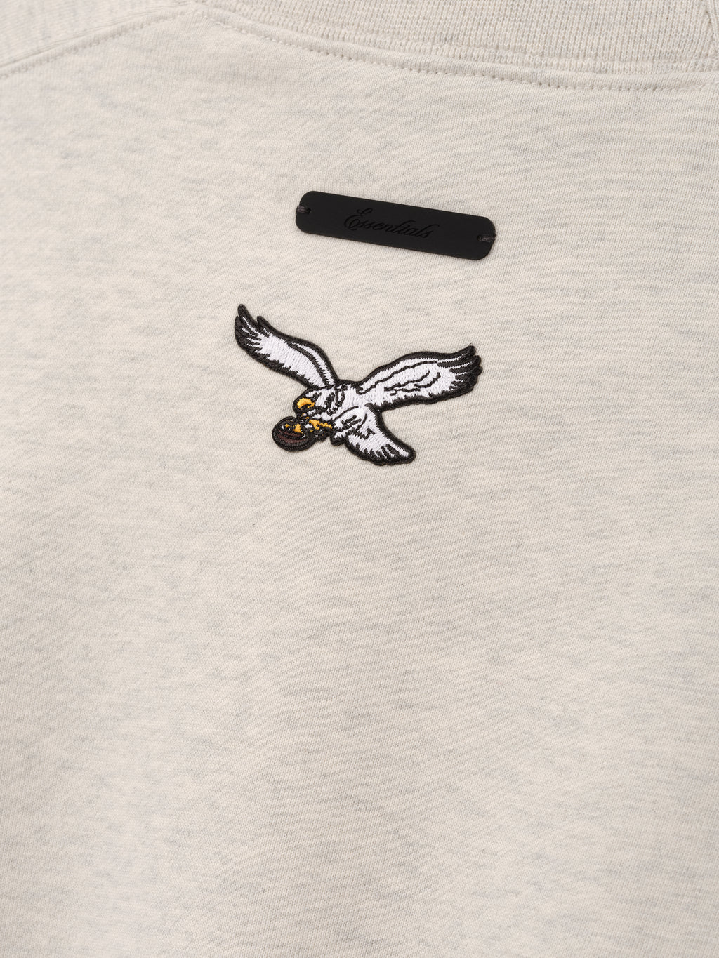 Eagles 90s Relaxed Crewneck cream sweatshirt close up featuring an embroidered flying eagle emblem and black label in a detailed Tops product view
