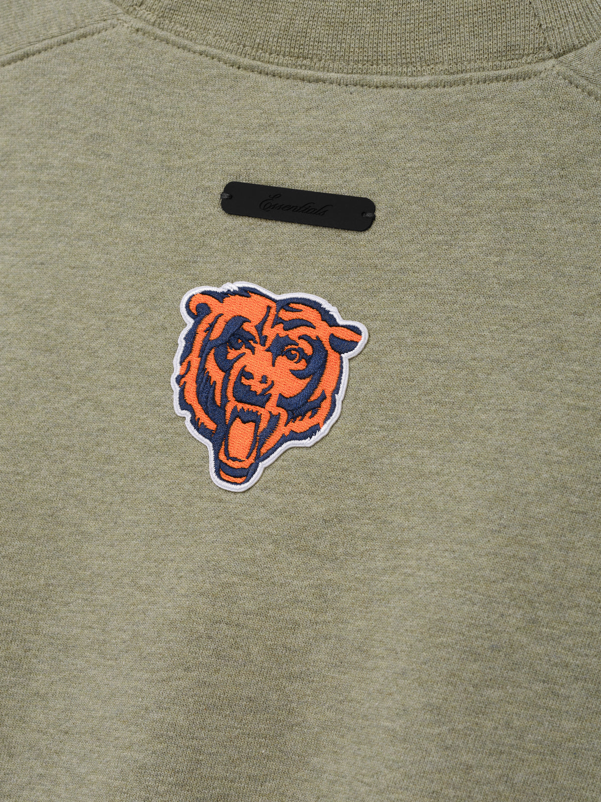 Bears 90s Relaxed Crewneck olive green sweatshirt close up with embroidered Chicago Bears head logo and black chest label shown in a detailed Tops product view