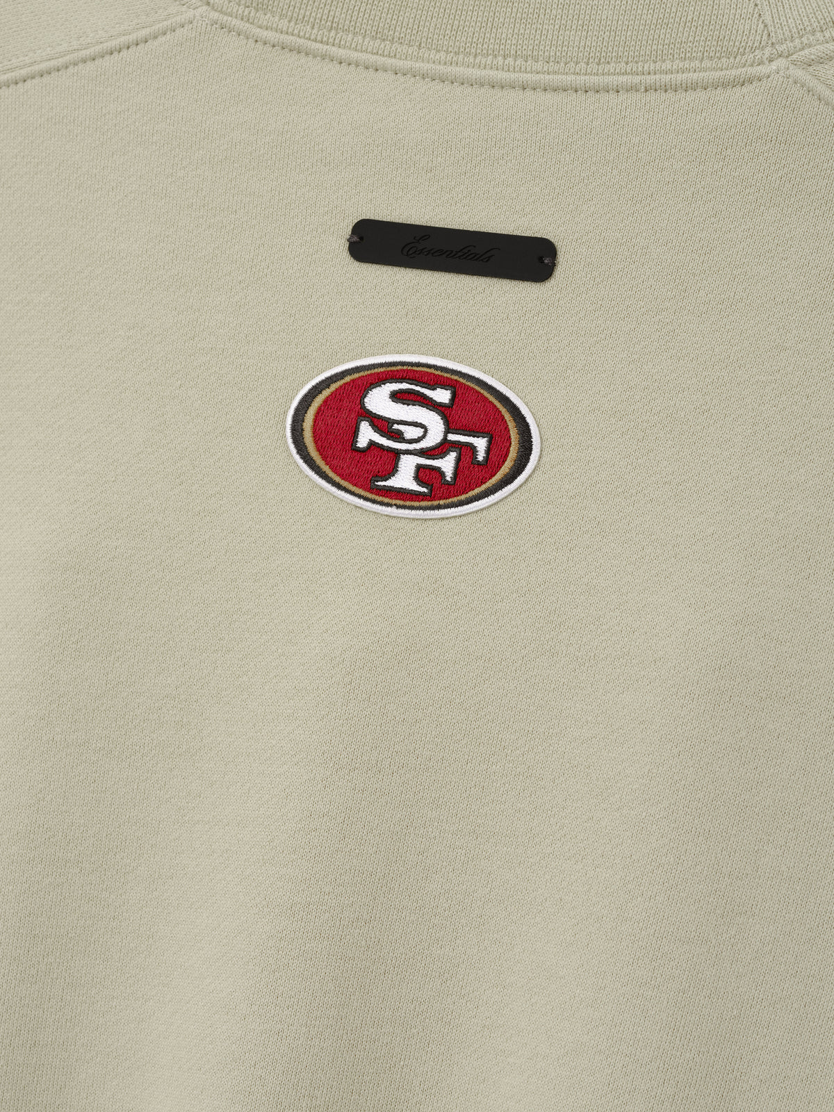 49ers 90s Relaxed Crewneck cream sweatshirt close up with embroidered San Francisco 49ers logo and black chest label shown as a Tops product detail