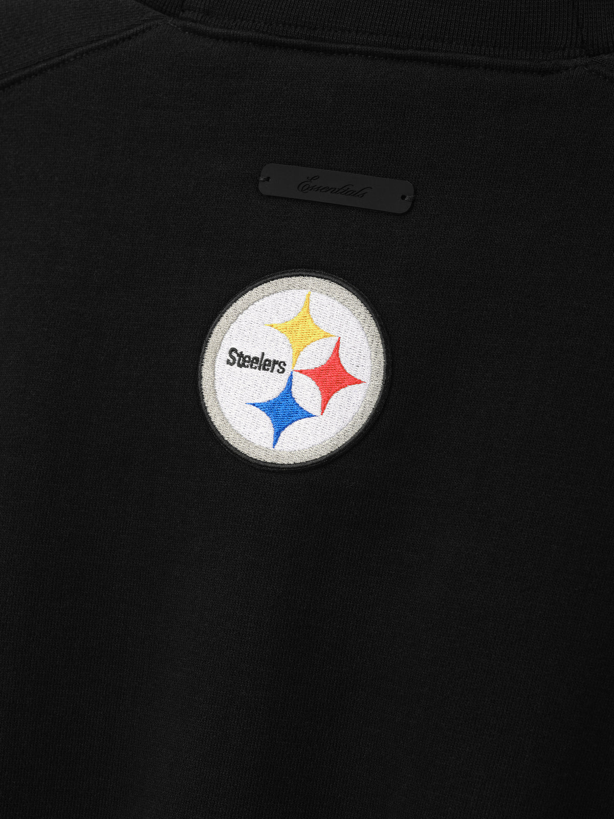 Steelers 90s Relaxed Crewneck black sweatshirt close up with embroidered Pittsburgh Steelers logo and subtle chest label shown as a Tops product detail