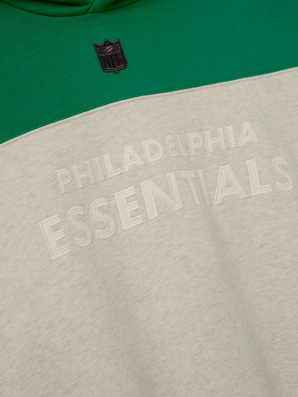 Eagles 90s Relaxed Hoodie close up showing green and cream color blocking black NFL shield and raised Philadelphia Essentials lettering as a Tops product detail