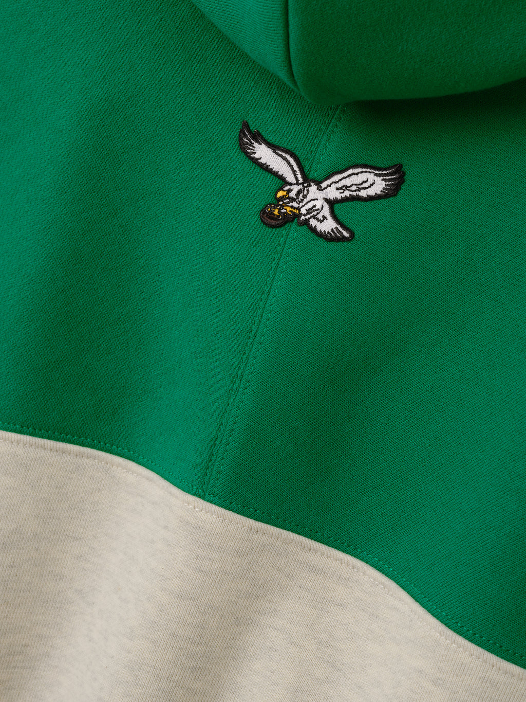 Eagles 90s Relaxed Hoodie close up showing an embroidered flying eagle logo on green fabric above cream color blocking as a Tops product detail