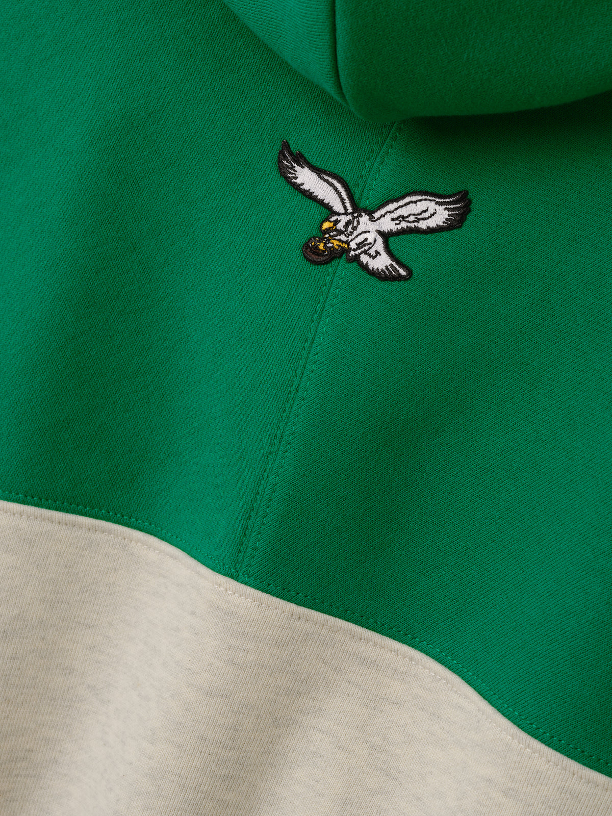 Eagles 90s Relaxed Hoodie close up showing an embroidered flying eagle logo on green fabric above cream color blocking as a Tops product detail