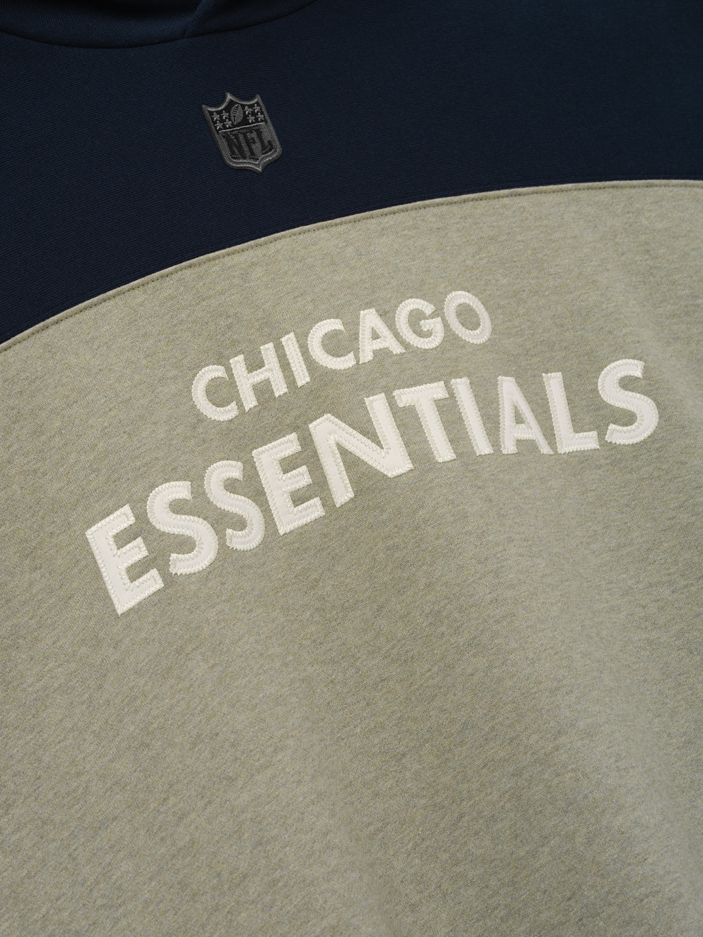 Bears 90s Relaxed Hoodie close up of navy and khaki color blocking with NFL shield and raised Chicago Essentials lettering as a Tops product detail