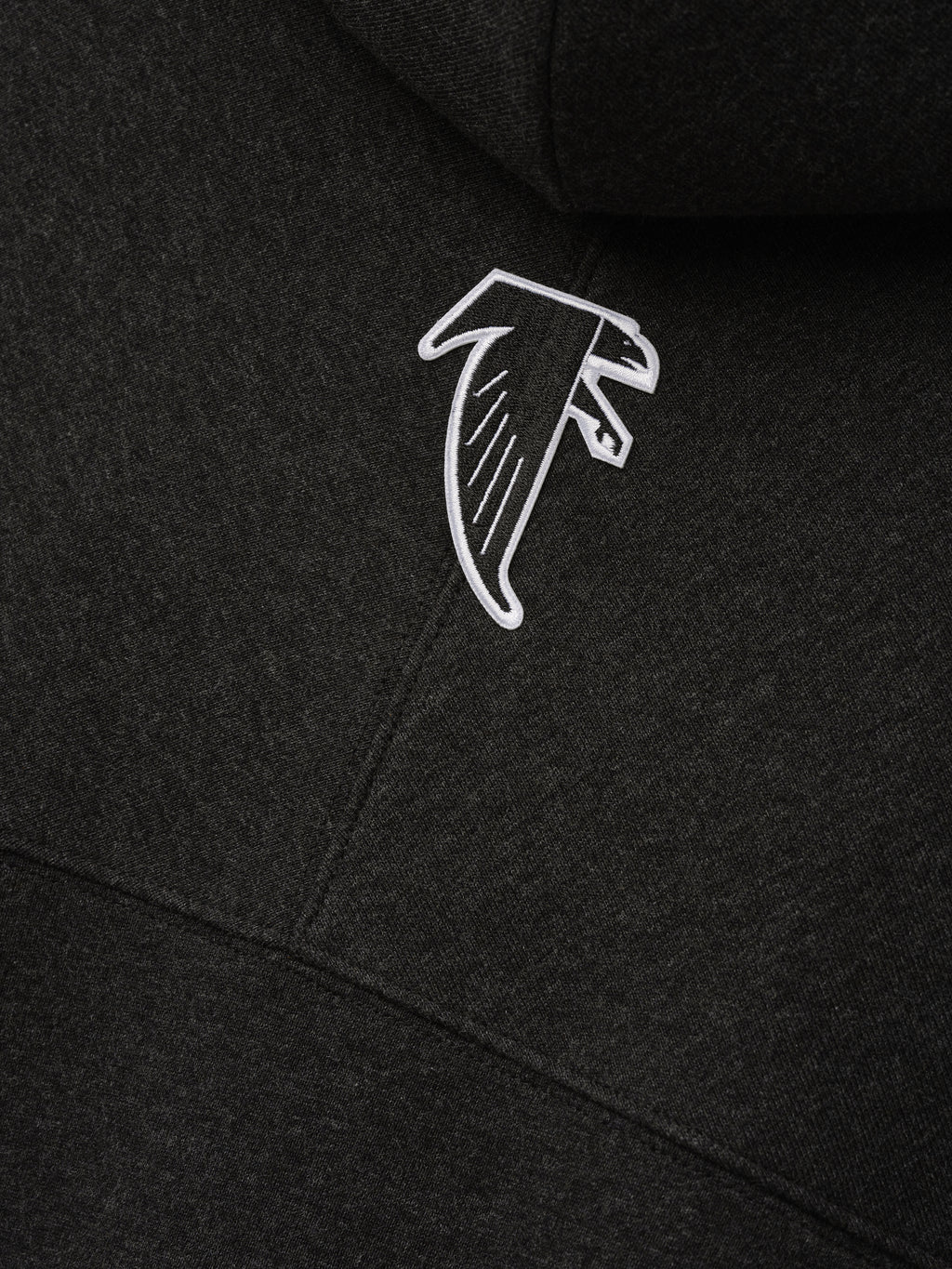 Falcons 90s Relaxed Hoodie close up in black with an embroidered white Atlanta Falcons logo on soft fleece fabric as a Tops product detail