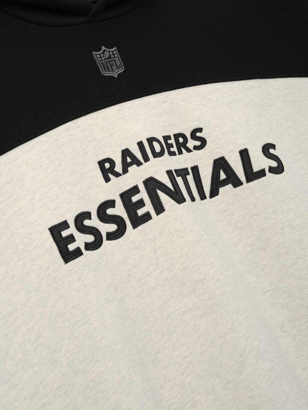 Raiders 90s Relaxed Hoodie close up showing black Raiders Essentials lettering and NFL shield on a cream and black front as a Tops product detail