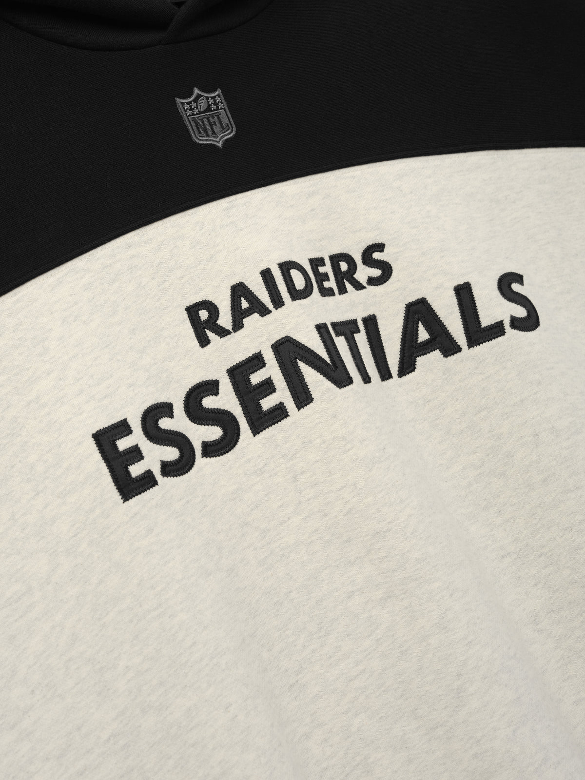 Raiders 90s Relaxed Hoodie close up showing black Raiders Essentials lettering and NFL shield on a cream and black front as a Tops product detail