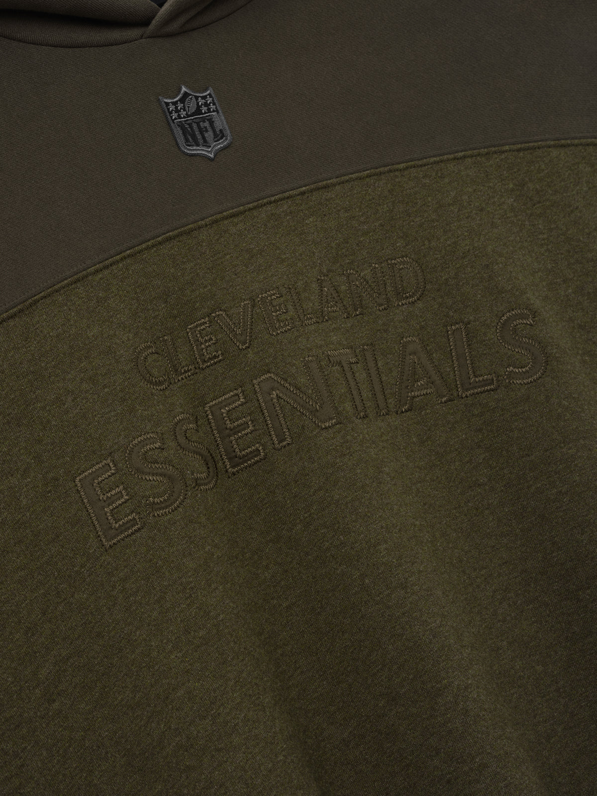 Browns 90s Relaxed Hoodie close up showing tonal Cleveland Essentials lettering and NFL shield on dark brown fleece with a curved color blocked seam as a Tops product detail