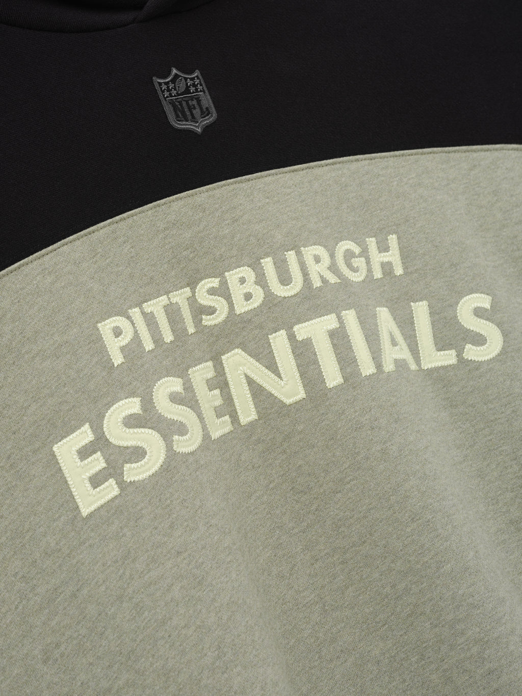 Steelers 90s Relaxed Hoodie close up featuring Pittsburgh Essentials lettering and NFL shield on black and gray fleece as a Tops product detail