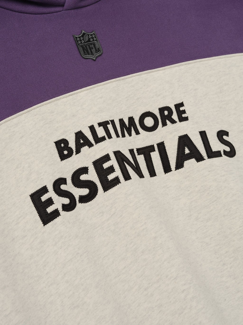 Ravens 90s Relaxed Hoodie close up with Baltimore Essentials lettering and NFL shield on purple and cream fleece as a Tops product detail