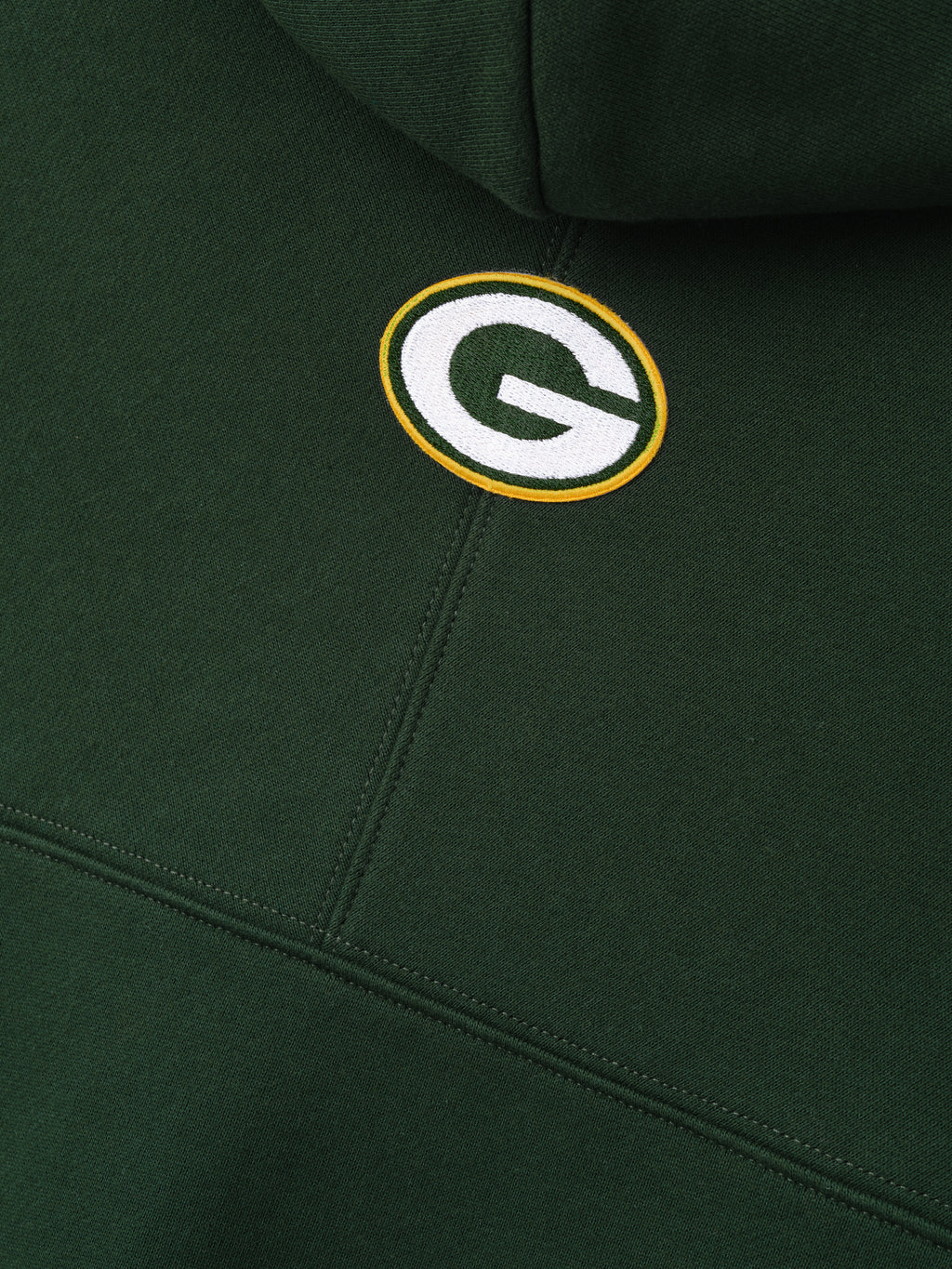 Packers 90s Relaxed Hoodie close up showing embroidered Green Bay Packers logo on dark green fleece with stitched panel seams as a Tops product detail