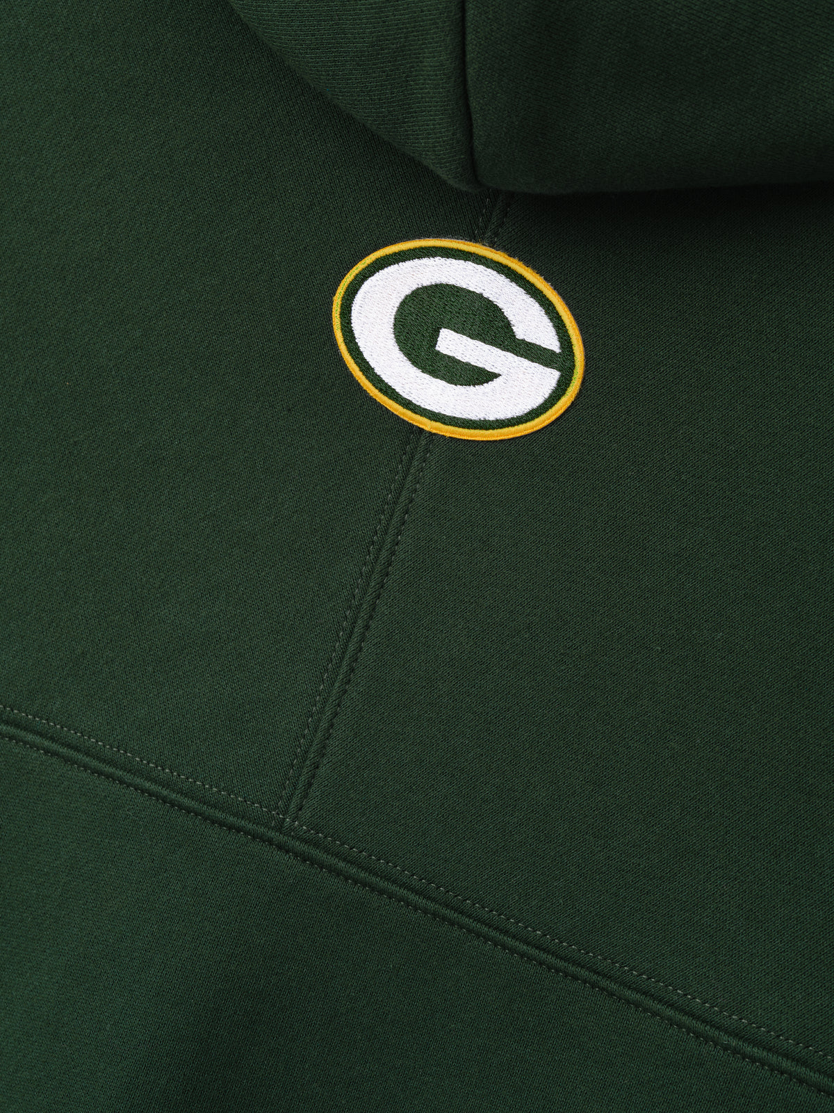 Packers 90s Relaxed Hoodie close up showing embroidered Green Bay Packers logo on dark green fleece with stitched panel seams as a Tops product detail