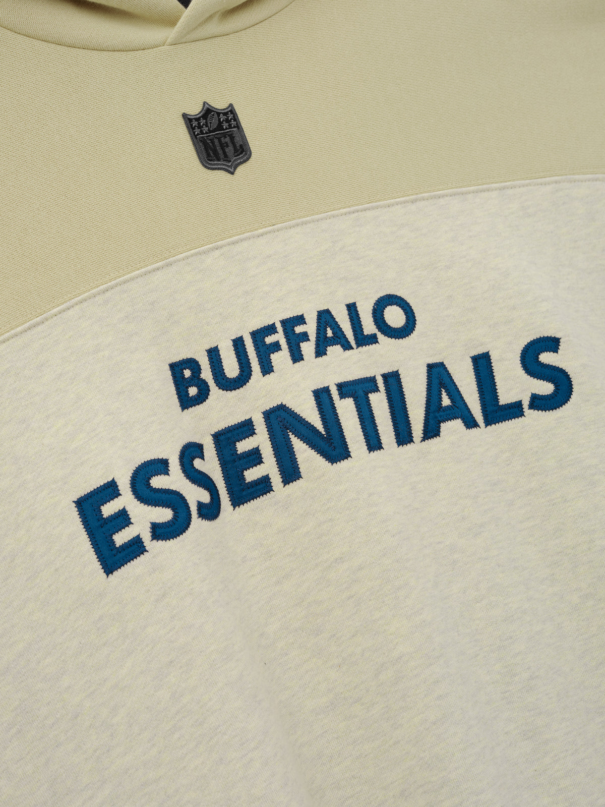 Bills 90s Relaxed Hoodie close up featuring Buffalo Essentials lettering and an NFL shield on cream color blocked fleece as a Tops product detail