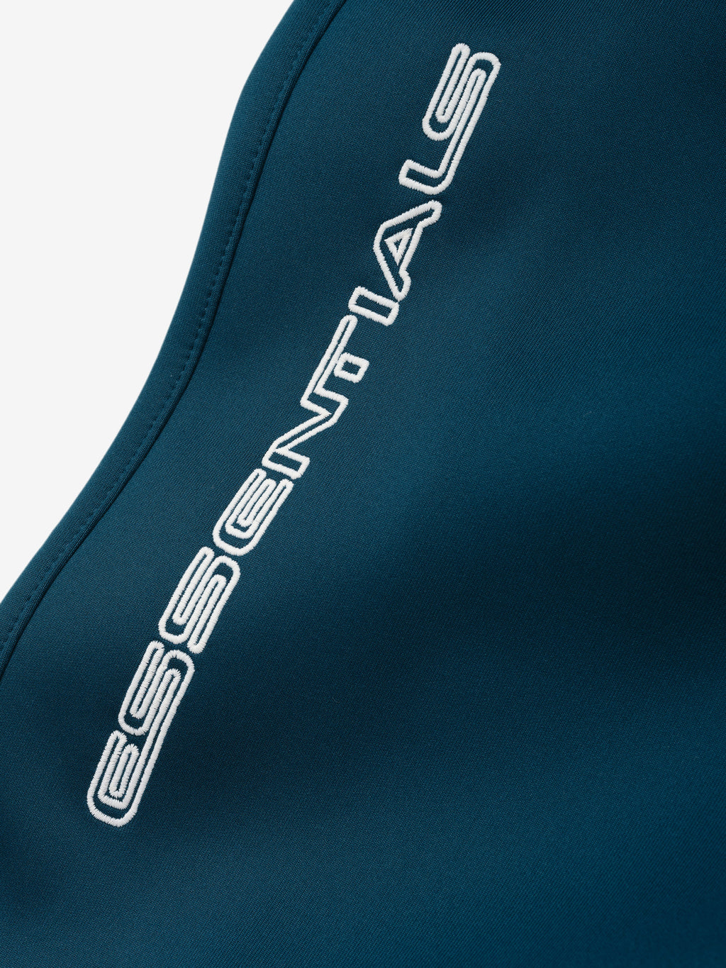 Tricot Classic Trackpant in deep teal with a close-up of the white ESSENTIALS logo along the side seam on smooth fabric as Bottoms