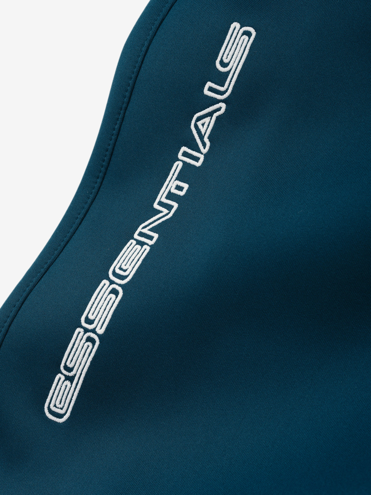 Tricot Classic Trackpant in deep teal with a close-up of the white ESSENTIALS logo along the side seam on smooth fabric as Bottoms