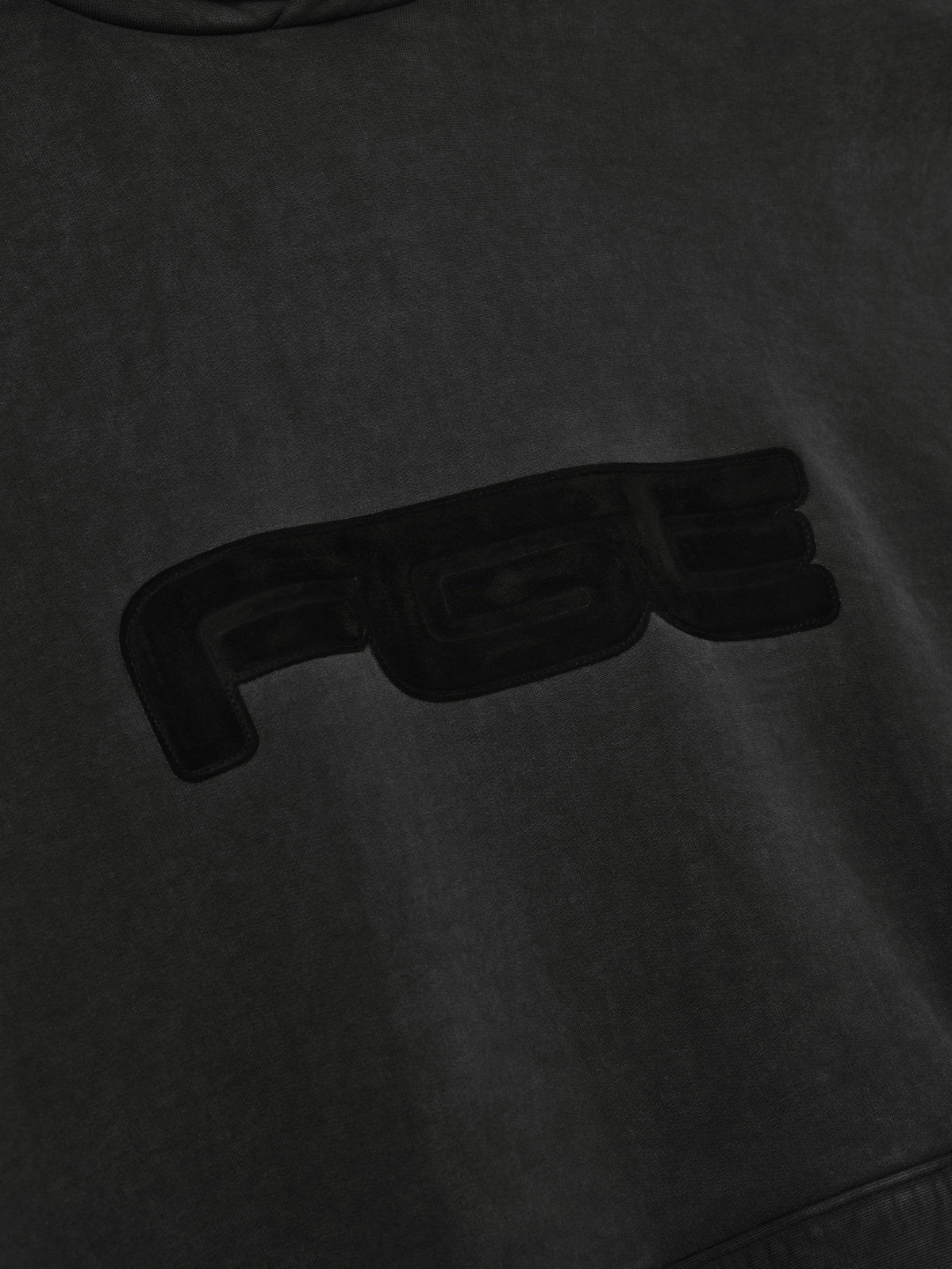 Slouchy 90s Hoodie in black shown close up with a tonal raised chest graphic and soft washed fabric texture Tops
