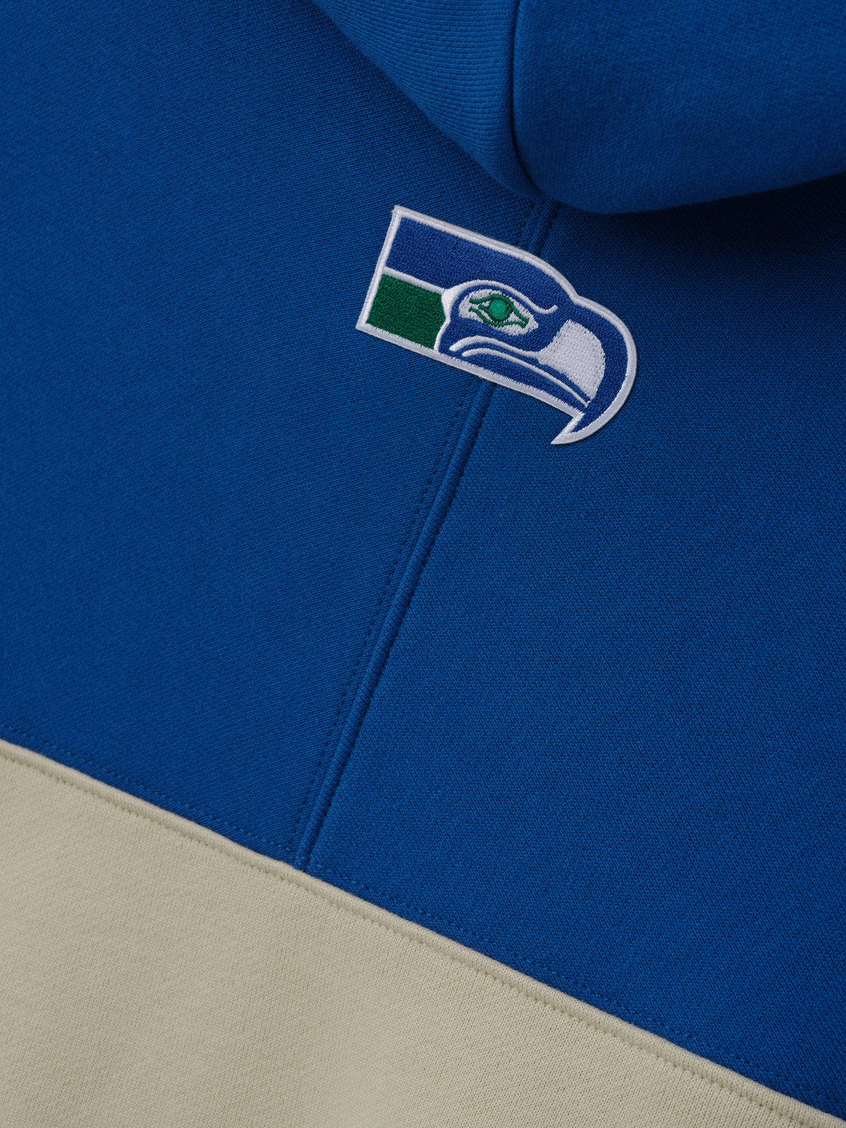 Seahawks 90s Relaxed Hoodie close up showing an embroidered Seahawks logo on blue and cream color block fleece with zip front detail as a Tops product view
