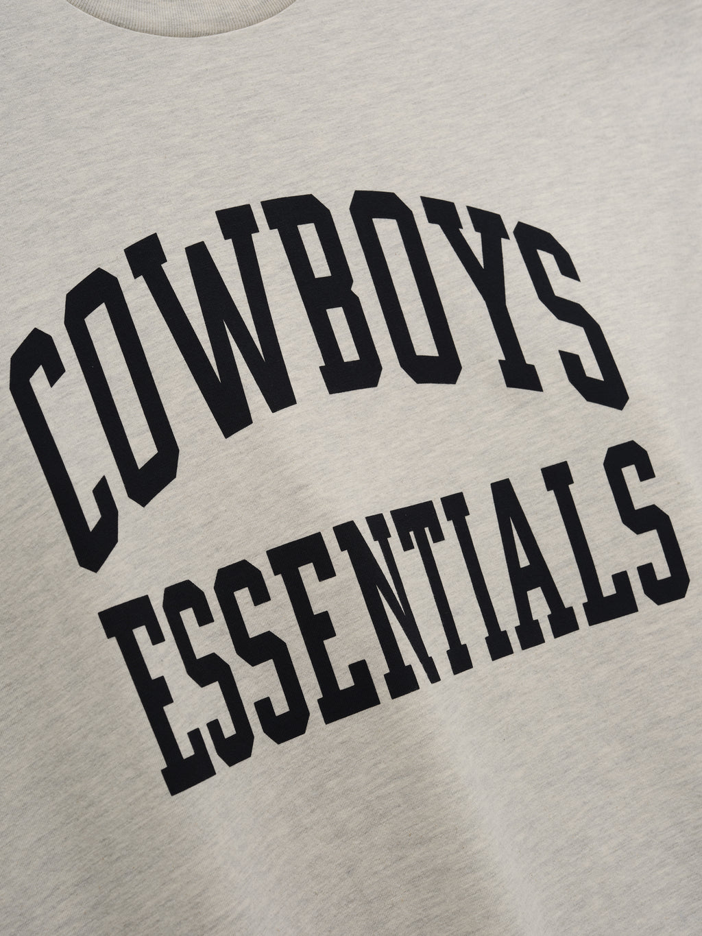 Dallas Cowboys Training Camp Tee in a light heather fabric with bold black collegiate-style "Cowboys Essentials" text printed across the chest on a soft casual top.
