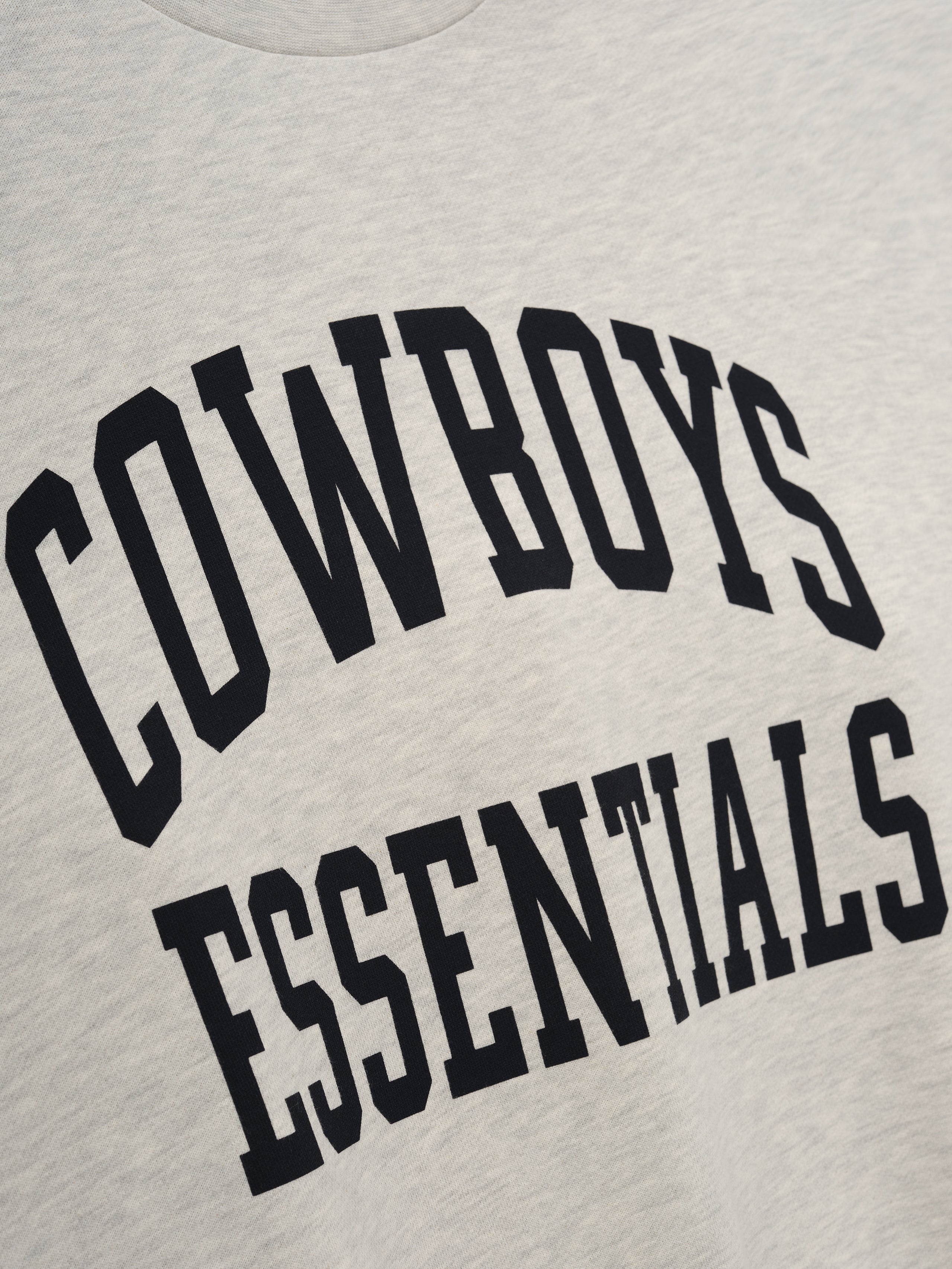 Dallas Cowboys Training Camp Crewneck Boxy Fit in light heather fabric featuring bold black collegiate-style "Cowboys Essentials" text on a soft casual top.