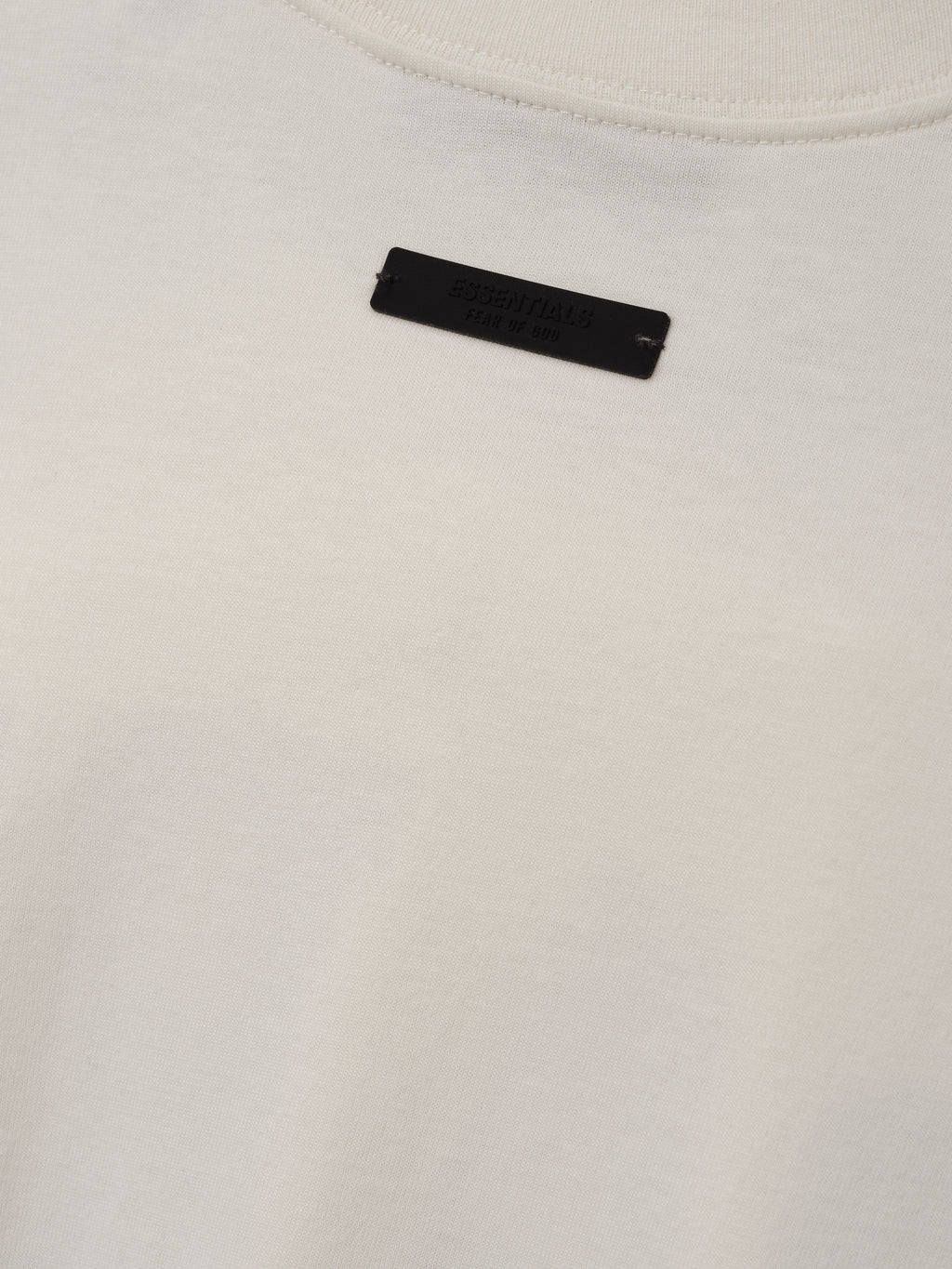 NFL Paris Merch Tee in off white with a ribbed crew neckline and black Fear of God label shown in close up Tops