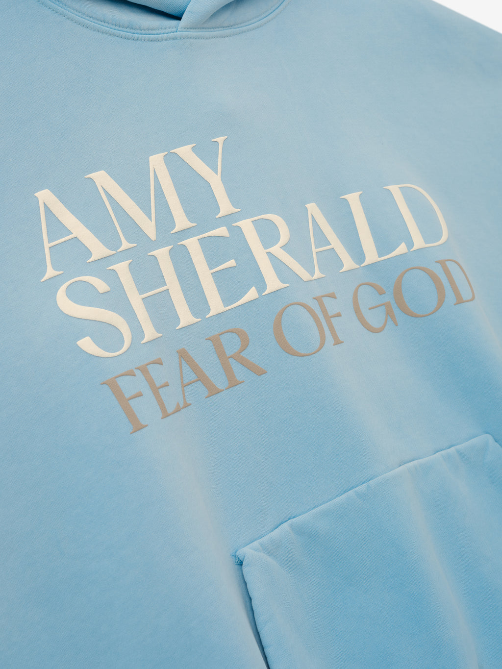 Fear of God Amy Sherald Pocket Hoodie in light blue with Amy Sherald Fear of God chest lettering and kangaroo pocket against a pale background Tops