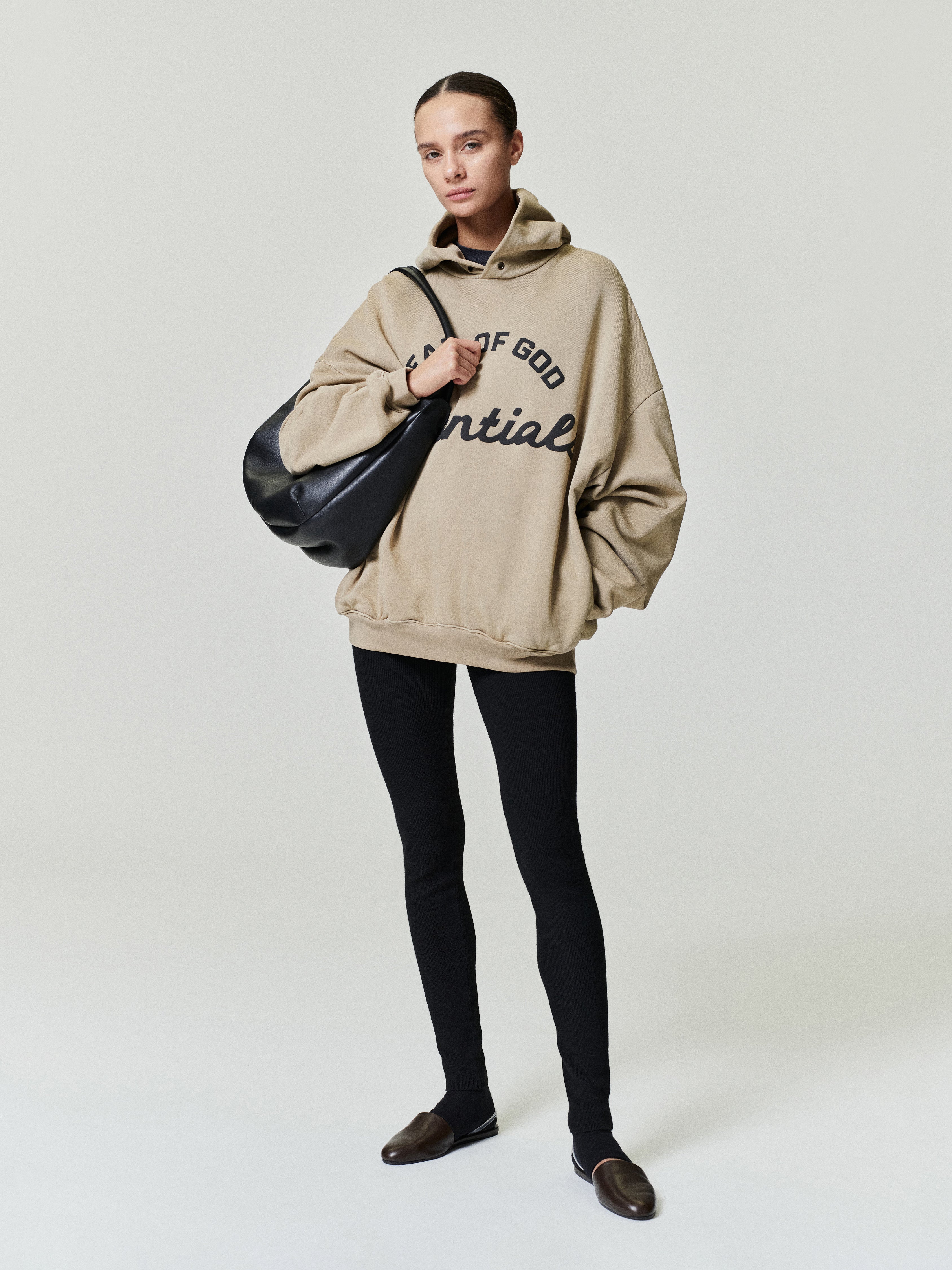 beige oversized 90s-inspired hoodie with puff-printed Essentials logo, styled with black leggings and brown shoes