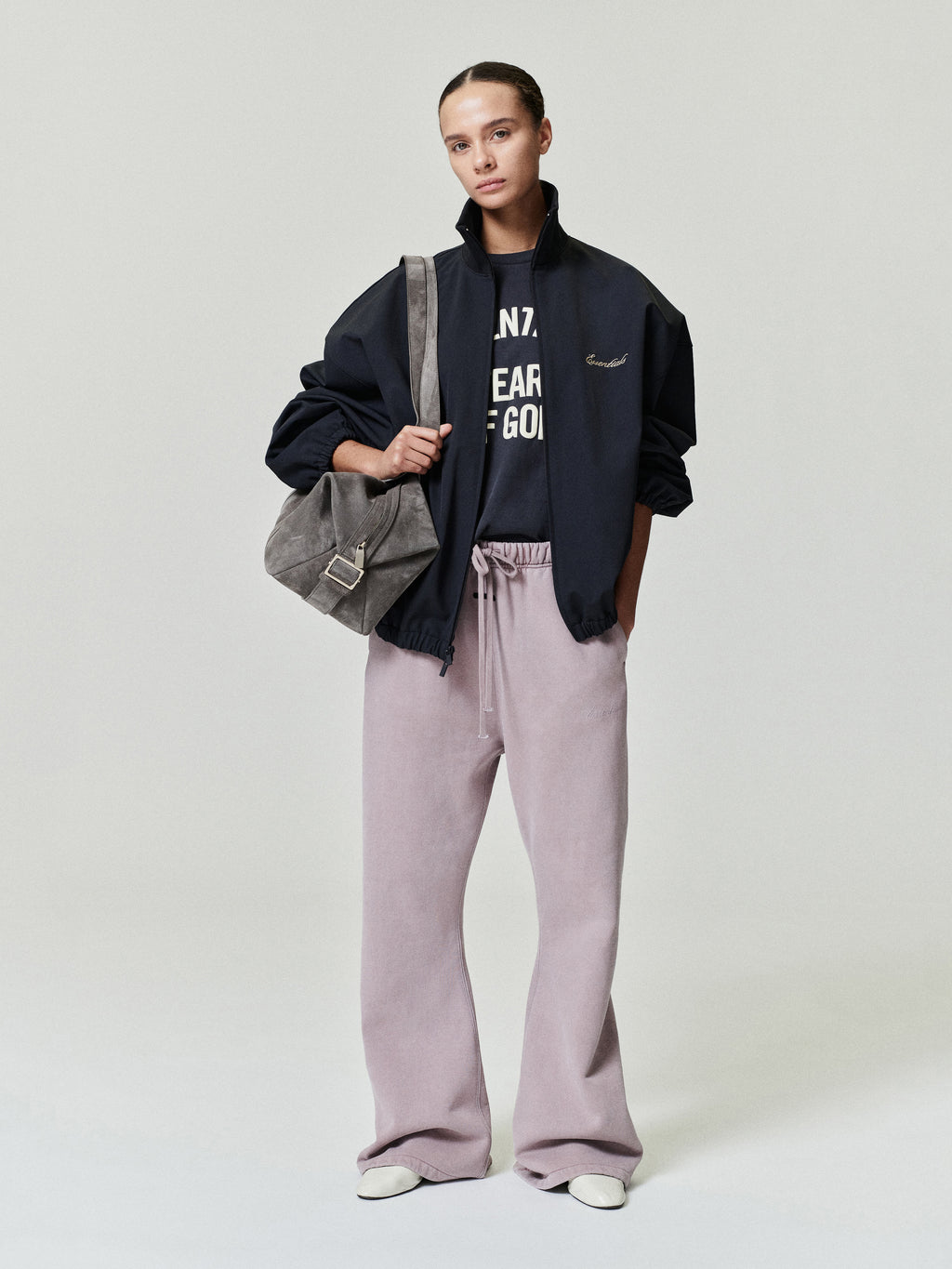 woman wearing black oversized zip-up jacket, graphic tee, lilac drawstring wide-leg pants, and carrying suede shoulder bag