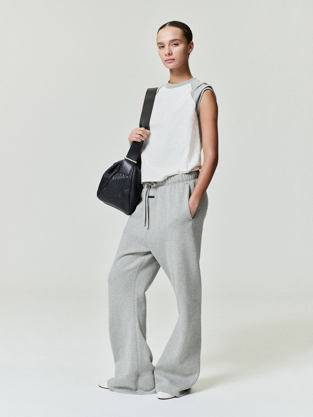 woman wearing sleeveless white ribbed cotton baseball tee with classic fit and raw hem paired with gray sweatpants