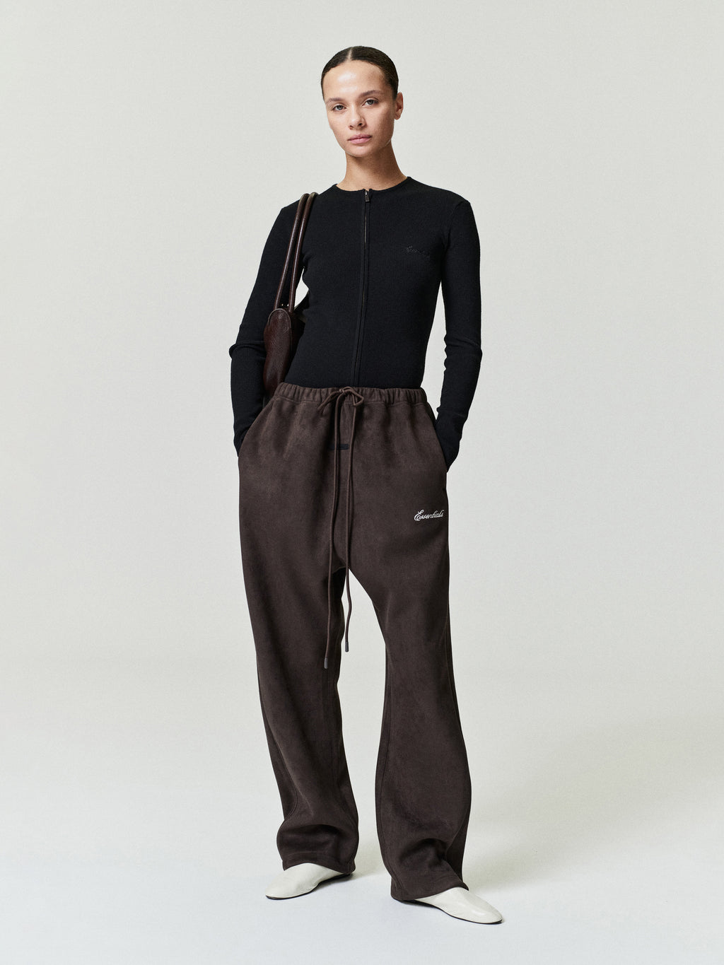 Person wearing a black top and brown pants with a visible brand logo on a white background