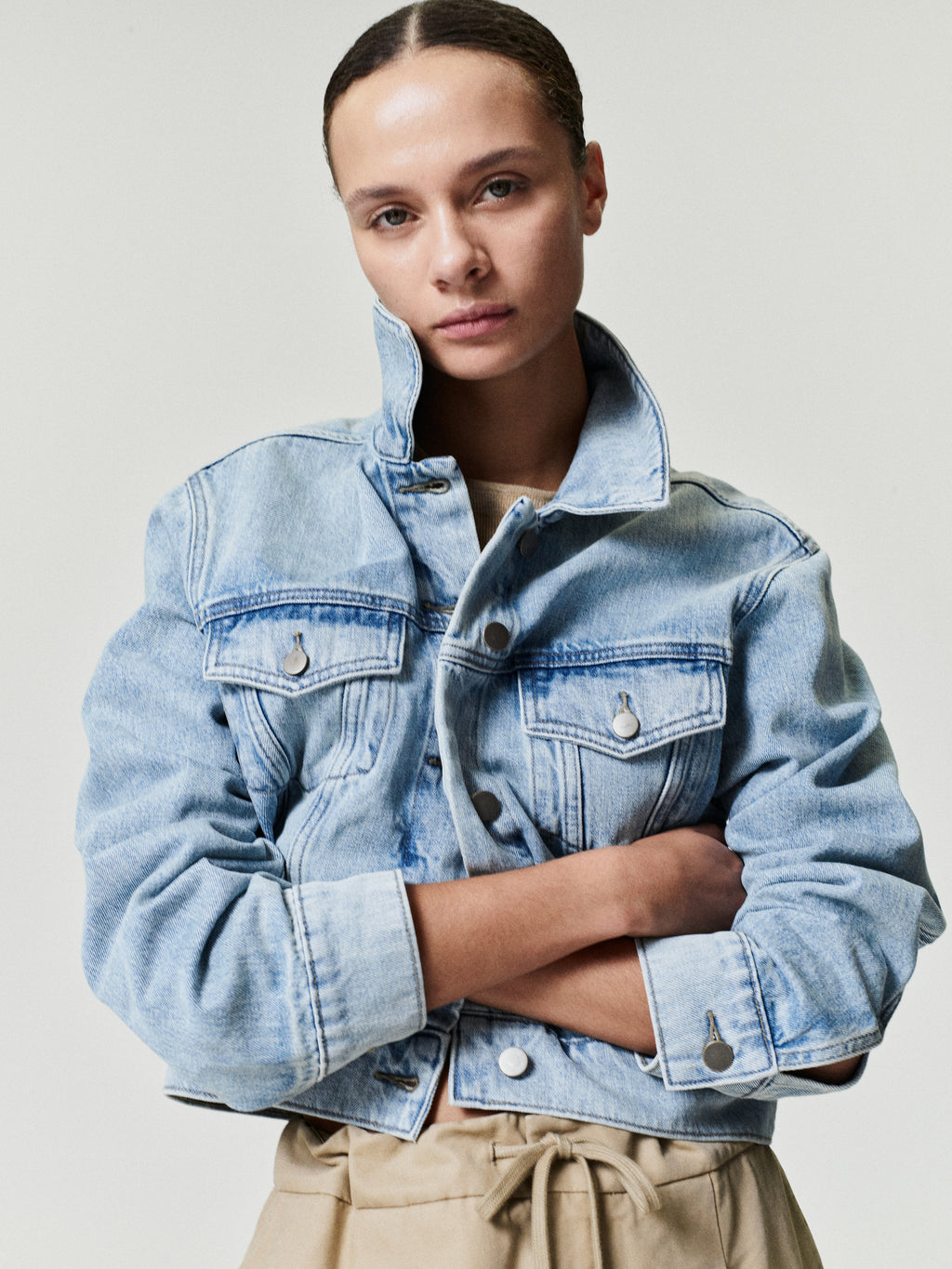 woman wearing light wash cropped denim trucker jacket with buttoned flap pockets and high collar