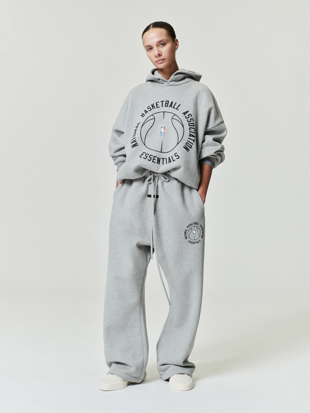 light grey heavyweight hoodie and matching sweatpants with circular NBA Essentials basketball graphics worn by model