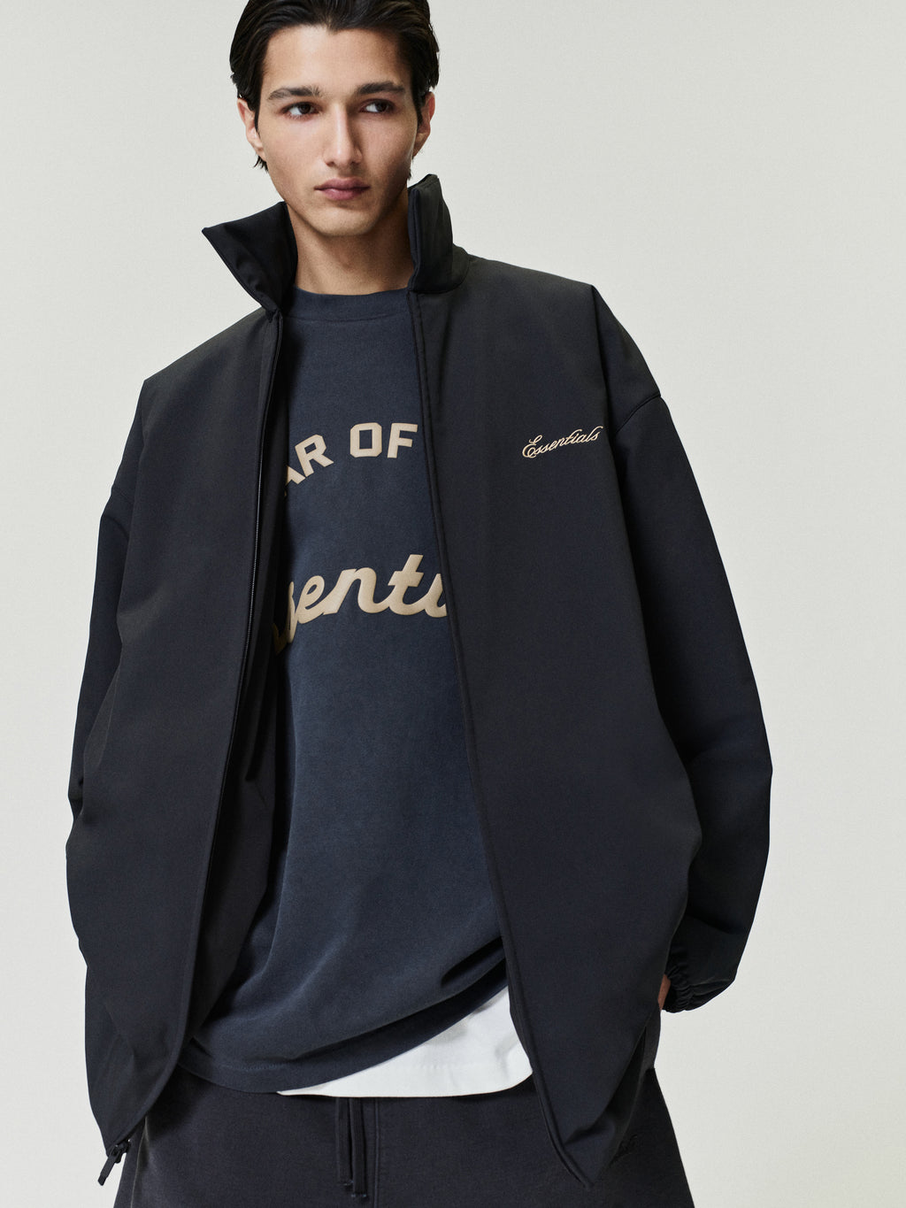 Man wearing a dark jacket over a branded sweatshirt on a plain background
